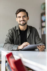 Lächelnder Mann mit Tablet-PC, der zu Hause am Tisch sitzt - PESF03611