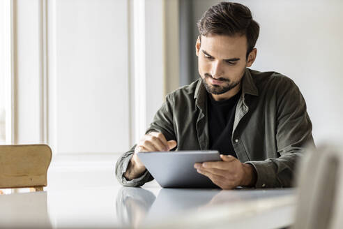 Mann sitzt am Tisch und benutzt einen Tablet-PC zu Hause - PESF03613