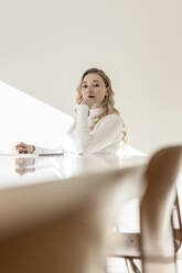 Confident woman with hand on chin sitting at table in apartment - PESF03631