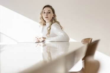 Young woman sitting on table at home on sunny day - PESF03632