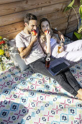 Mann und Frau essen einen Apfel auf einer Picknickdecke auf einer Terrasse - PESF03637