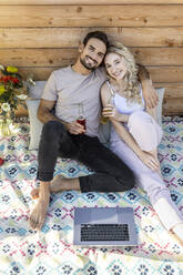 Man with arm around girlfriend sitting on picnic blanket - PESF03639