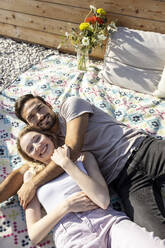 Paar umarmt sich auf einer Picknickdecke auf der Terrasse liegend - PESF03644