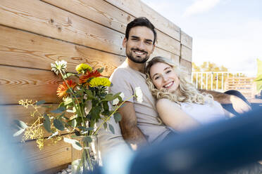 Glückliches Paar, das sich auf der Terrasse bei einer Blumenvase ausruht - PESF03646