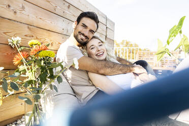 Man embracing girlfriend by flower vase on terrace - PESF03647
