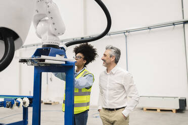 Ingenieur, der eine Roboterarm-Maschine analysiert, steht neben einem Geschäftsmann in einer Fabrik - JCCMF05764