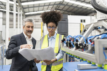 Businessman discussing over blueprint with engineer in factory - JCCMF05774