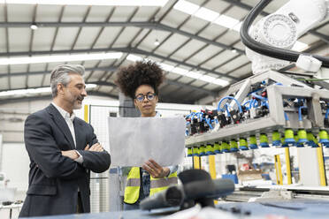 Engineer reading blueprint discussing with businessman in factory - JCCMF05775