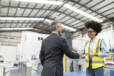 Happy businessman shaking hand with engineer in factory - JCCMF05780