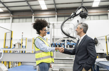 Smiling businessman shaking hand with engineer in factory - JCCMF05781