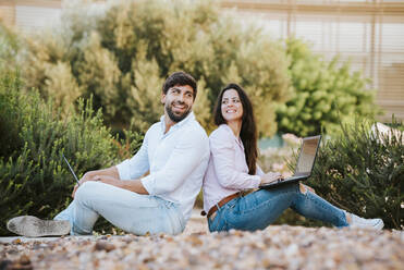 Happy freelancers sitting with laptops outdoors - MIMFF00765