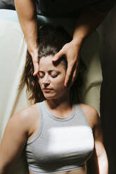 Physiotherapist giving head massage to woman lying with eyes closed - MIMFF00791
