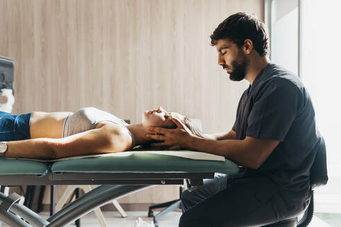 Physiotherapist doing head massage to woman at medical clinic - MIMFF00792