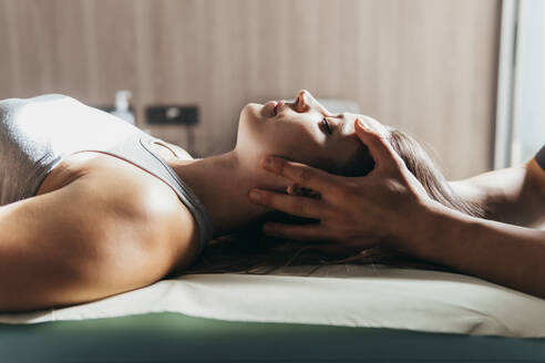 Woman with eyes closed getting head massage by physiotherapist at medical clinic - MIMFF00793