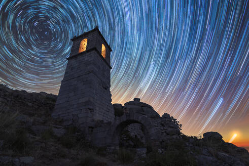 From below of aged stone tower with glowing lights located against starry sky with long exposure at night time in countryside - ADSF34068