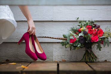 Faceless anonymous woman in white dress with red shoes in hand near flower composition against wooden wall - ADSF34117