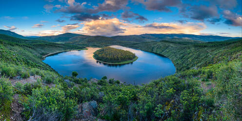 Atemberaubende Landschaft von Regenbogen über ruhigen Fluss fließt durch hügeliges Gelände gegen bewölkten blauen Himmel in Meandro Del Melero National Park in Spanien - ADSF34126