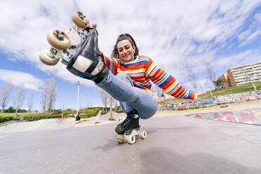 Smiling woman roller skating in skateboard park on sunny day - OCMF02349