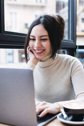 Lächelnde Geschäftsfrau mit Laptop in einem Café sitzend - PNAF03408