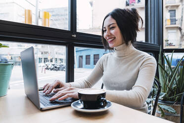 Glückliche Geschäftsfrau mit Laptop in einem Café sitzend - PNAF03412