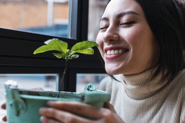 Lächelnde Frau mit geschlossenen Augen, die an einer Pflanze riecht - PNAF03419