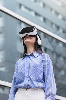 Lächelnde Frau in einem Virtual-Reality-Simulator an einem sonnigen Tag - PNAF03436