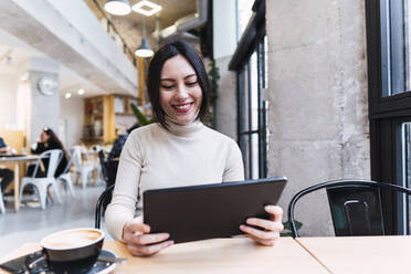 Happy woman holding tablet PC sitting at cafe - PNAF03441