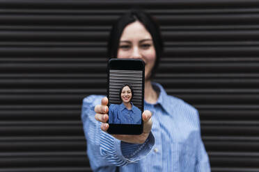 Woman showing photo through smart phone in front of shutter - PNAF03444