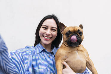 Glückliche Frau mit Hund, der die Zunge herausstreckt, vor einer Wand - PNAF03451