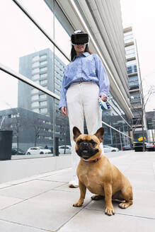 Glückliche Geschäftsfrau im Virtual-Reality-Simulator mit Hund auf dem Gehweg - PNAF03456