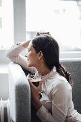 Glückliche Geschäftsfrau, die eine Kaffeetasse hält und mit der Hand im Haar am Arbeitsplatz sitzt - JOSEF07674