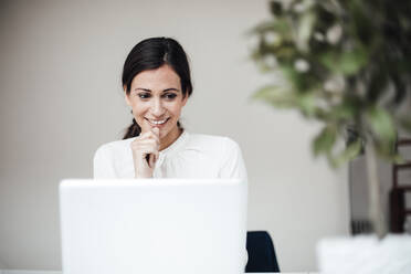 Smiling businesswoman sitting with laptop in office - JOSEF07677