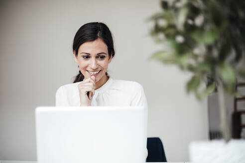 Lächelnde Geschäftsfrau sitzt mit Laptop im Büro - JOSEF07677