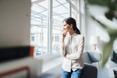 Smiling businesswoman looking through window in office - JOSEF07684