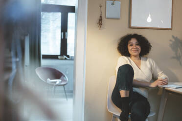 Smiling woman with coffee cup and tablet PC sitting on chair at home - JOSEF07699