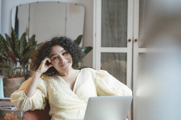 Happy woman with laptop sitting with head in hand home - JOSEF07727