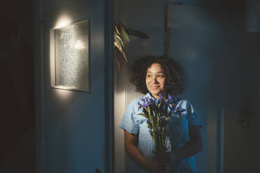 Lächelnde Frau mit Blumen an der Wand lehnend zu Hause - JOSEF07729