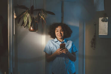 Woman holding mobile phone standing at home - JOSEF07730