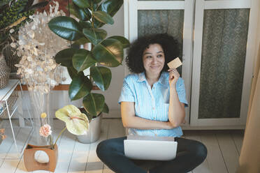 Nachdenkliche Frau mit Kreditkarte und Laptop beim Online-Shopping zu Hause - JOSEF07753
