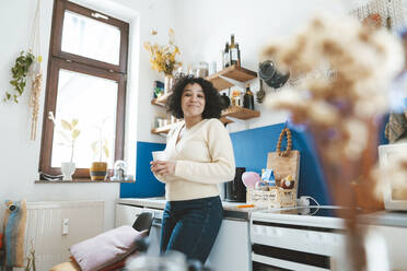 Lächelnde Frau mit Kaffeetasse in der Küche zu Hause stehend - JOSEF07762