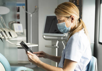 Zahnarzt mit Gesichtsschutzmaske bei der Arbeit mit einem Tablet-PC in einer Zahnklinik - JCCMF05801