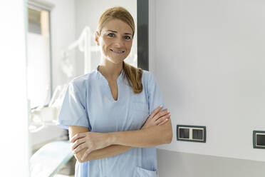 Smiling dentist standing with arms crossed in dental clinic - JCCMF05815