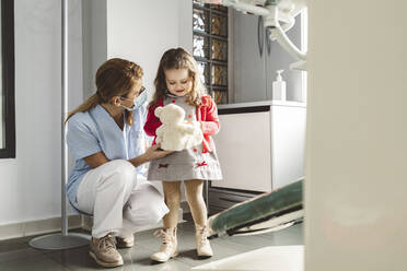 Dentist with cute little girl holding stuffed toy at dental clinic - JCCMF05817