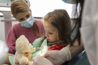 Dentist making cute little girl comfortable for examining at dental clinic - JCCMF05842