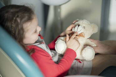 Little girl sitting on dental chair with stuffed toy at medical clinic - JCCMF05858