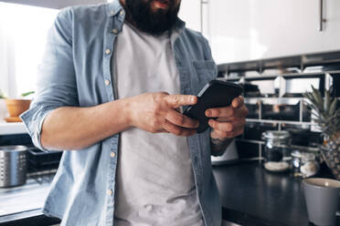 Man using smart phone in kitchen at home - ASGF02214