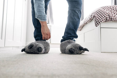 Man wearing wolf paw slippers in bedroom at home - ASGF02232