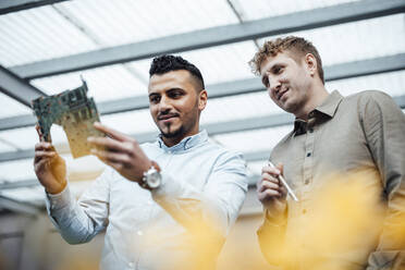 Businessman with colleague analyzing circuit board at work place - JOSEF07819