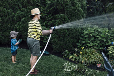 Grandmother with grandson watering plants in garden - ACTF00174