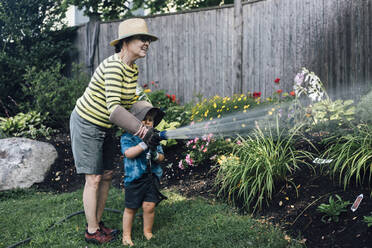 Glückliche Großmutter mit Enkel, die gemeinsam Pflanzen im Garten gießen - ACTF00175